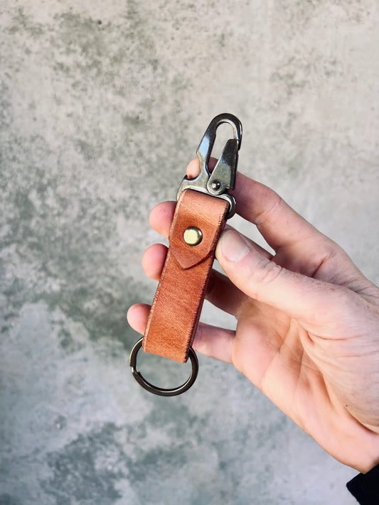 Hand holding a brown leather keychain with a metal ring against a gray concrete background